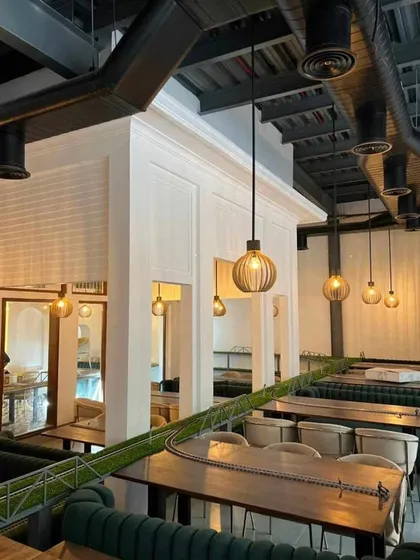 An interior view of a themed restaurant project we completed. This shot highlights the unique dining setup with custom seating, industrial-style overhead ducting, and thematic elements like the miniature railway, showcasing our capability in commercial interior design.