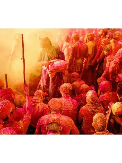 A crowd of devotees, drenched in red and yellow hues, celebrate with fervor. This shot captures the collective spirit and energy of the participants.