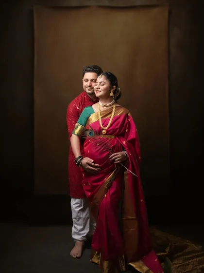 A classic portrait celebrating tradition. The rich red saree and his kurta create a vibrant, warm image. Their comfortable embrace and serene expressions make this a beautiful memory of their pregnancy journey.