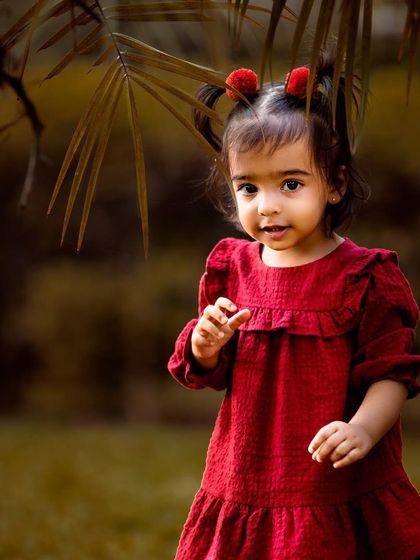 This little girl in her cute red dress looks so sweet against the lush green background. Outdoor toddler photography is perfect for capturing their curious and adventurous spirit in a natural environment.