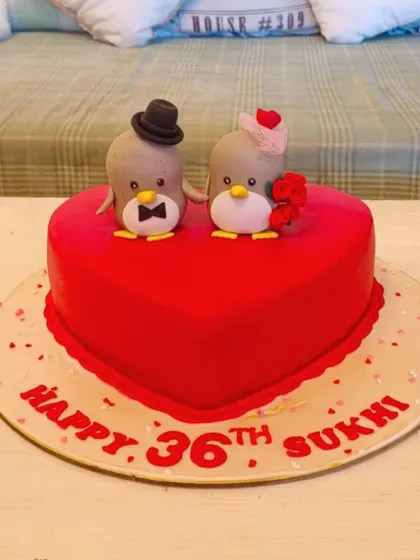 An adorable heart-shaped anniversary cake topped with two cute fondant penguins in love.