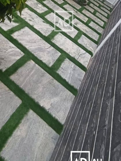 This outdoor flooring design combines large stone pavers with strips of artificial grass. It creates a modern, geometric pattern that is low-maintenance and visually interesting.