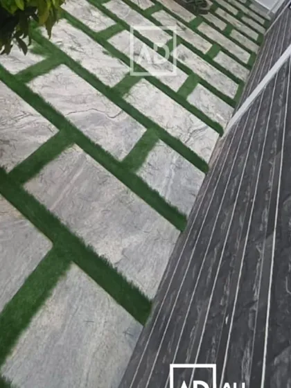 This outdoor flooring design combines large stone pavers with strips of artificial grass. It creates a modern, geometric pattern that is low-maintenance and visually interesting.