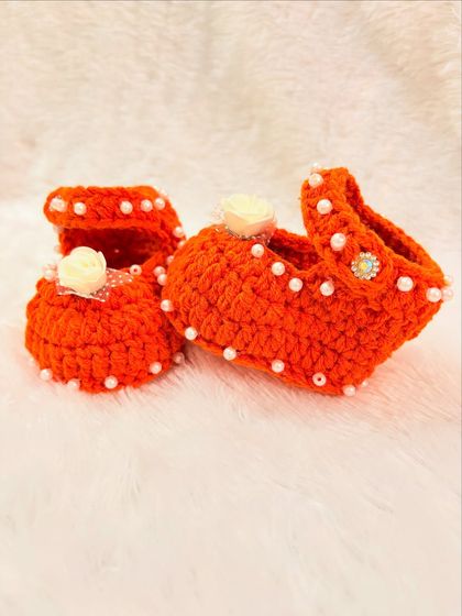 A side view of the orange Mary Jane-style booties, showing the strap and the pretty pearl and flower details.