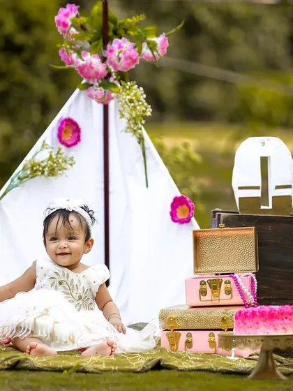 A beautiful shot of the birthday girl sitting in her outdoor setup, surrounded by flowers, balloons, and decorative cases, creating a whimsical picnic vibe.