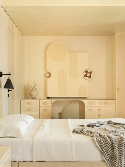 The master suite in the 'Soft Serve' project is enveloped in a timeless taupe. The custom bed and vanity feature abstract patterns in Movingue White veneer, with scalloped motifs framing the bay window.