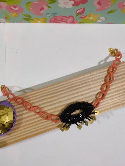 This western-style choker features a black beaded ring with golden tassels on a peach-colored chain. It's a modern and chic accessory for a night out.