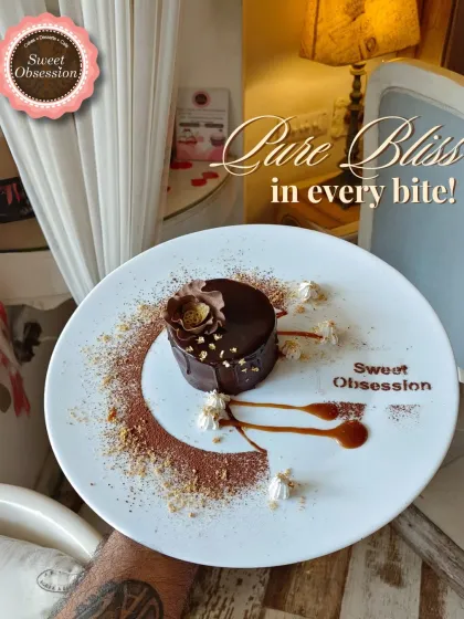 Pure bliss in every bite. This elegantly plated chocolate dessert features a rich mousse cake, artfully decorated with cocoa powder and caramel sauce for a grand finale to your meal.