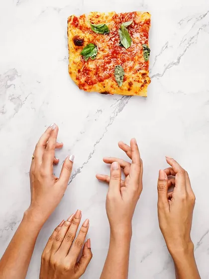 A conceptual flatlay with a single slice of pizza and multiple hands reaching for it. This artistic shot plays with minimalism and desire, perfect for a creative ad campaign.