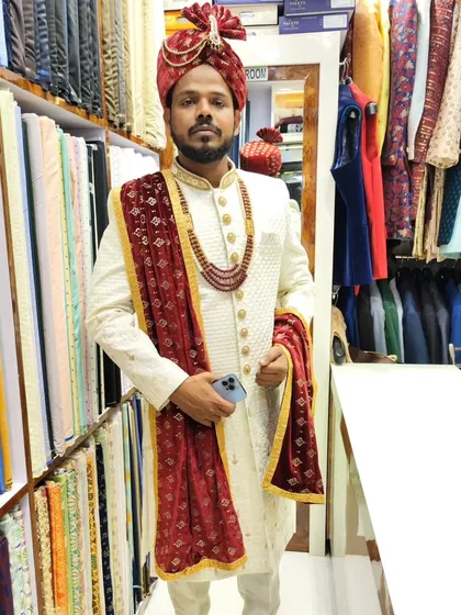 A happy groom in his classic white sherwani, paired with a rich maroon stole and pagdi. This timeless combination is perfect for a traditional wedding ceremony.