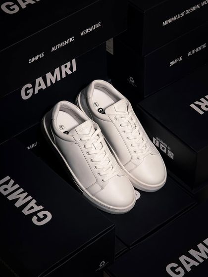 Classic white sneakers displayed on top of branded black shoeboxes. The high contrast and sharp lighting give this a premium, clean look.