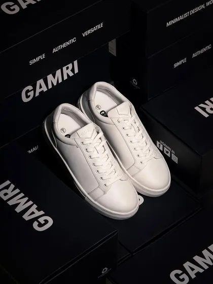 A clean, high-end shot of white leather sneakers surrounded by branded boxes. The dark, moody lighting and sharp focus convey a sense of premium quality and exclusivity.