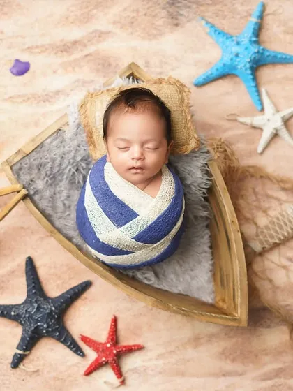 A little sailor dreaming of the sea. This newborn is swaddled in a nautical-themed wrap and placed in a tiny boat, surrounded by sand and starfish.