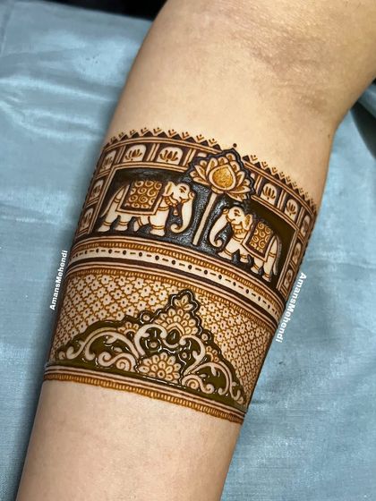 A close-up of the elephant procession arm band in progress. The dark henna paste highlights the intricate details of this classic motif.