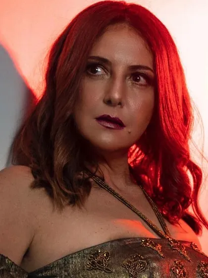 A close-up beauty shot with dramatic red lighting. The makeup features a bold, vampy lip and smokey eyes, creating an intense and captivating look.