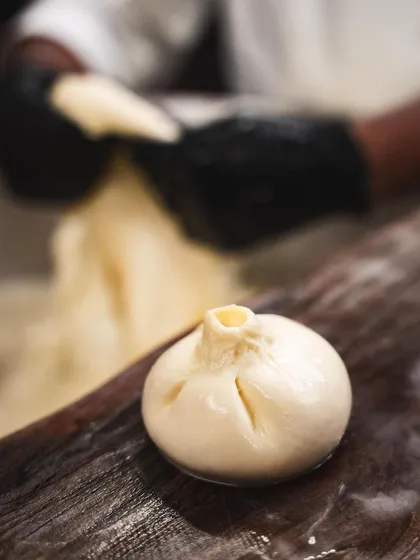 A freshly formed burrata, with its signature top knot, resting on a wooden board before being filled with stracciatella.