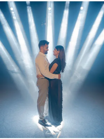 A couple stands in the spotlight, literally, surrounded by dramatic beams of light for a cinematic and theatrical pre-wedding photo.