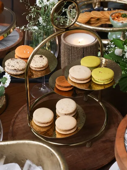 The Tête-à-tête high tea stand, a four-tiered statement piece in stainless steel gold. Here it is, beautifully arranged with macarons, showcasing its elegance and capacity.