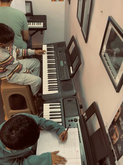 Students practicing during a keyboard class. One student is playing while another works on theory, showing our balanced approach to practical skills and theoretical knowledge.