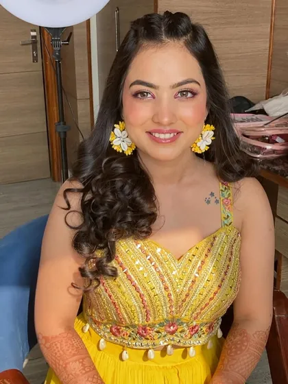 A stunning Haldi look with a pop of color on the eyes. The pink eyeshadow and fresh, dewy skin perfectly complement the yellow outfit and floral earrings.