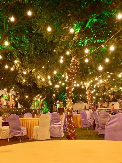A beautiful outdoor seating area under a canopy of trees wrapped in fairy lights. This simple yet effective lighting creates a whimsical and romantic setting for guests to dine and celebrate.