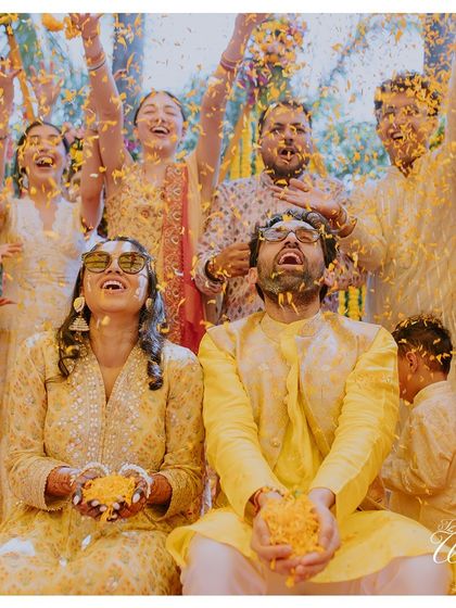 A moment of pure, unadulterated joy. The couple and their friends are showered in a sea of yellow marigold petals during a fun-filled Haldi ceremony.