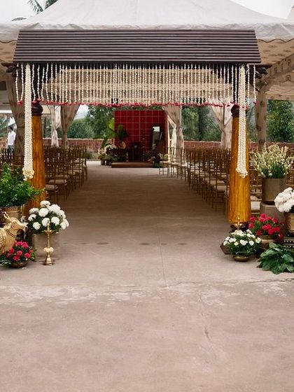The entrance to a traditional ceremony. The walkway is lined with an array of flowers and vintage brass props, including a beautiful brass cow statue, leading to a tented mandap area.