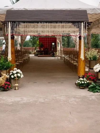 The entrance to a traditional wedding ceremony, where guests are greeted by an aisle flanked with beautiful brass decor, fresh flowers, and a view of the mandap.