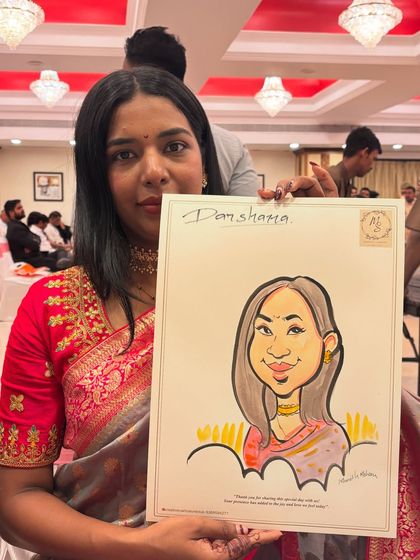 A guest in a lovely saree holds her caricature, which captures the elegance of her attire and jewelry.