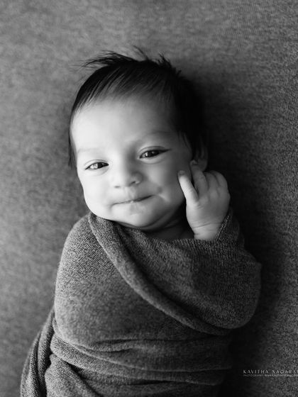 A newborn gives a sweet smile, captured in a beautiful black and white portrait. This style perfectly highlights the light, the emotion, and the moment.