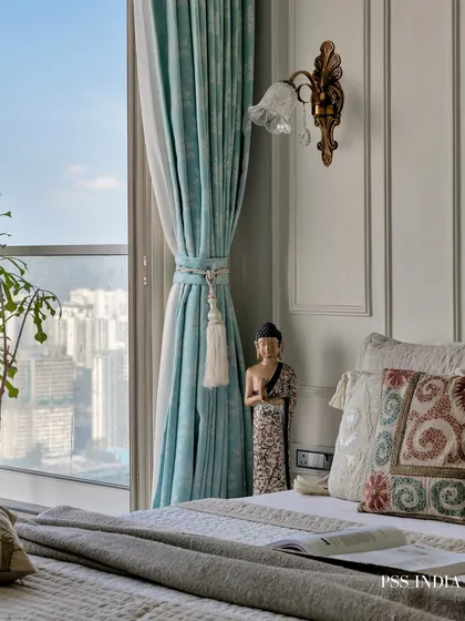A small Buddha statue and a book rest on the bedside table, adding a personal and spiritual touch. The view of the city skyline through the window provides a stunning backdrop.