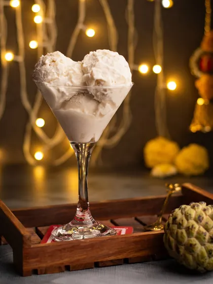 A festive shot of Sitaphal ice cream in a martini glass, set against a backdrop of Diwali lights. It's a modern way to serve a traditional flavor.