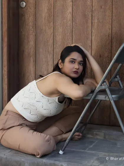 A close-up of the model leaning on a chair, with a direct and engaging expression.