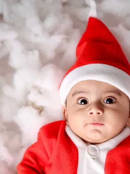 A beautiful close-up portrait of a baby in a Santa hat, with wide, curious eyes looking at the festive surroundings.