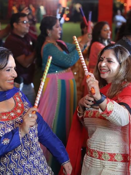Happy faces all around. Two ladies enjoying the live Dandiya session, dancing with their sticks and smiling. This is the joy we aim to create.