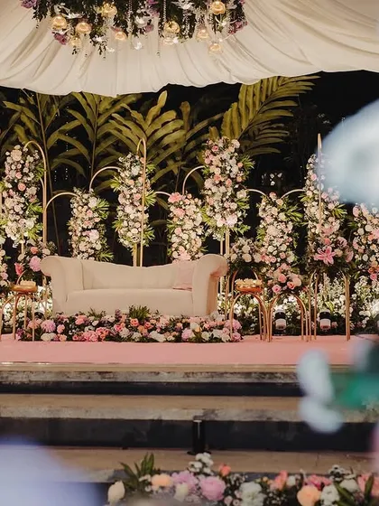 A dreamy reception stage setup in hues of pink and white. We used elegant gold arches adorned with beautiful floral arrangements and a classic white sofa to create a romantic and sophisticated photo corner for the couple.