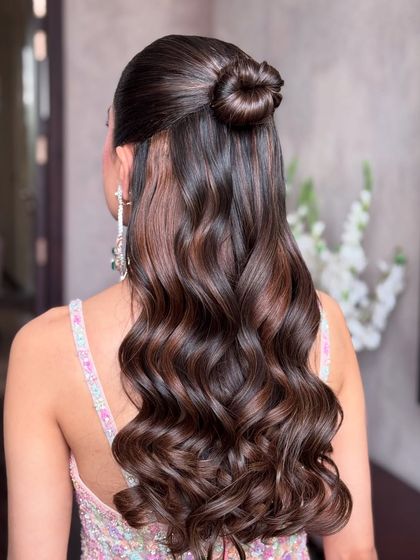 A close-up of the glamorous half-up style with a sleek top knot and flowing curls.