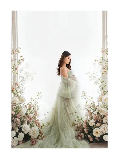 A full-length portrait showcasing a dreamy, ethereal look. The soft green gown and floral frame create a picture of a mother-to-be in her own secret garden.