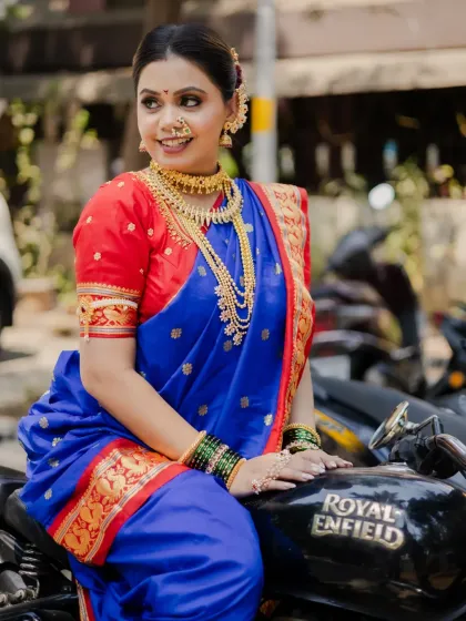 A bold and stylish portrait combining tradition with a modern edge. The model sits confidently on a Royal Enfield motorcycle, her vibrant Paithani saree creating a striking contrast.