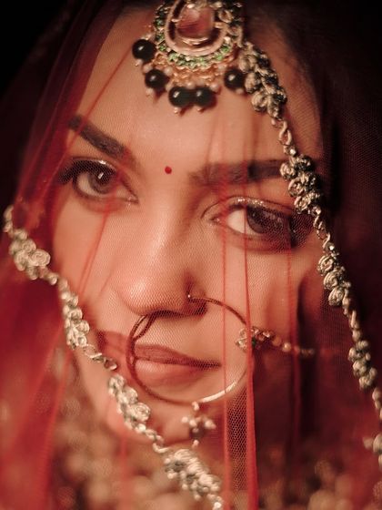 An intense close-up of a bride's eyes, looking directly at the camera through her sheer red dupatta.