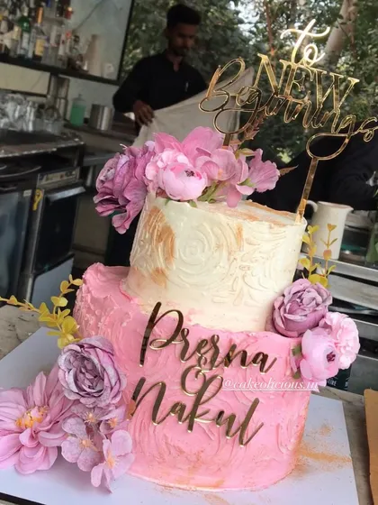 A pretty two-tier engagement cake for a new beginning. The bottom tier has a pink textured finish, while the top is a classic white with gold stenciling, all brought together with beautiful pink flowers and custom name toppers. The flavor was a crowd-pleasing white forest.