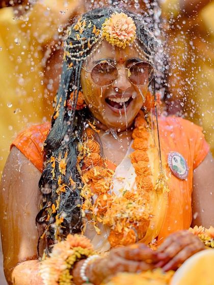 The bride gets a refreshing splash of water during her Haldi, her expression one of pure, unadulterated joy.