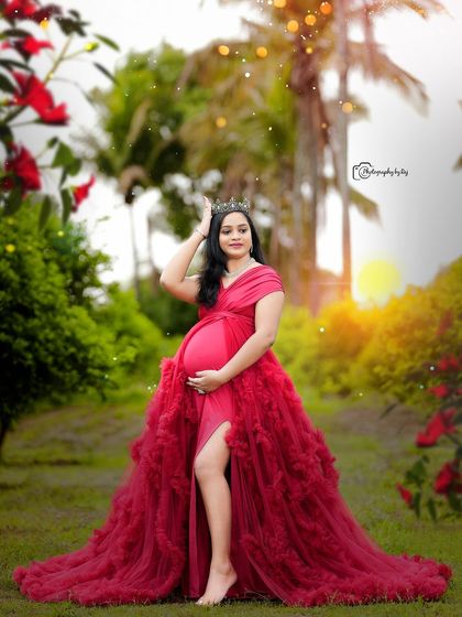 A regal portrait of a mother-to-be in a red ruffled gown and crown, looking absolutely radiant.