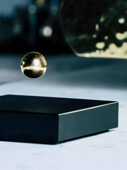 The Buda Ball in a luxurious gold finish, floating above its base on a sleek marble surface. This version adds a touch of warmth and opulence, making it a sophisticated decorative accent for a modern home or executive office.
