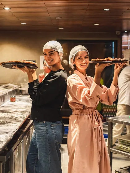 Two happy customers posing with the pizzas they made themselves at our workshop.