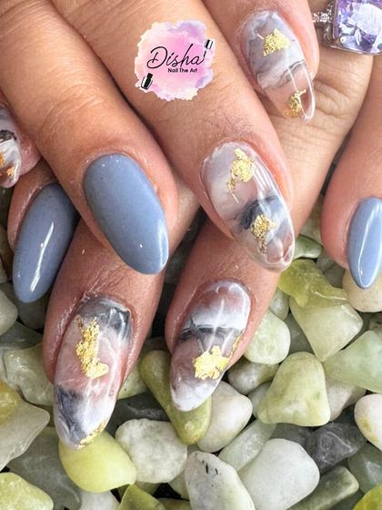 When the nails and the background complement each other. This design features a mix of solid grey-blue and a stone-like marble effect with gold foil.