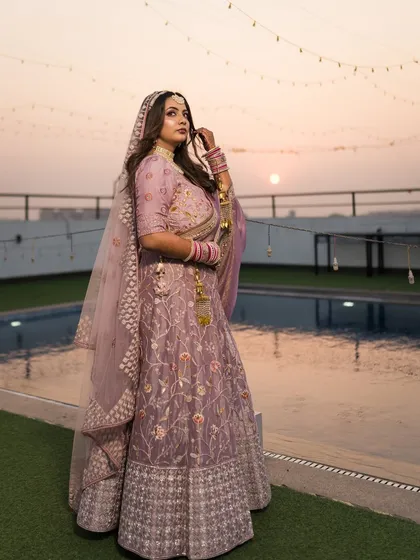 A full-length portrait of the bride, Nitika, showcasing her stunning lilac lehenga against the sunset sky.