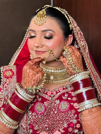 A beautiful moment as the bride adjusts her nose ring. This shot shows the detailed henna, the traditional red chooda, and her glowing makeup.