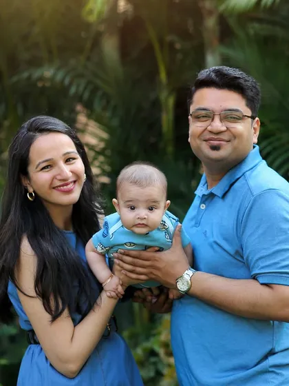 A happy family of three enjoying an outdoor photoshoot. The coordinated blue outfits look great against the green background, creating a fresh and vibrant family portrait.