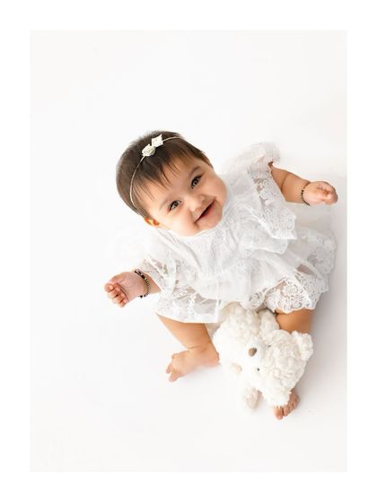 Looking up with the sweetest grin. This high angle shot in a delicate white lace outfit emphasizes her innocence and joy. It’s a beautiful way to remember how small they once were.